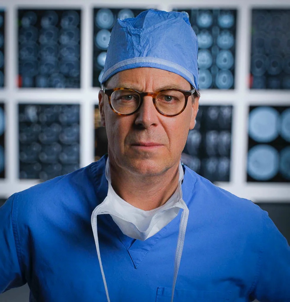Brian Hoeflinger in surgical scrubs standing in front of medical scans
